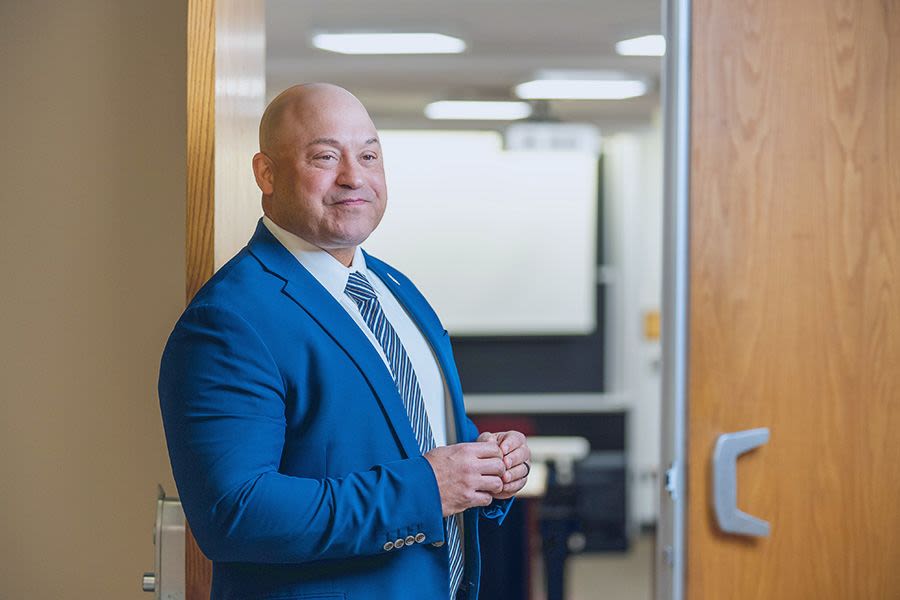 Professor Burton stands in front of an open classroom door